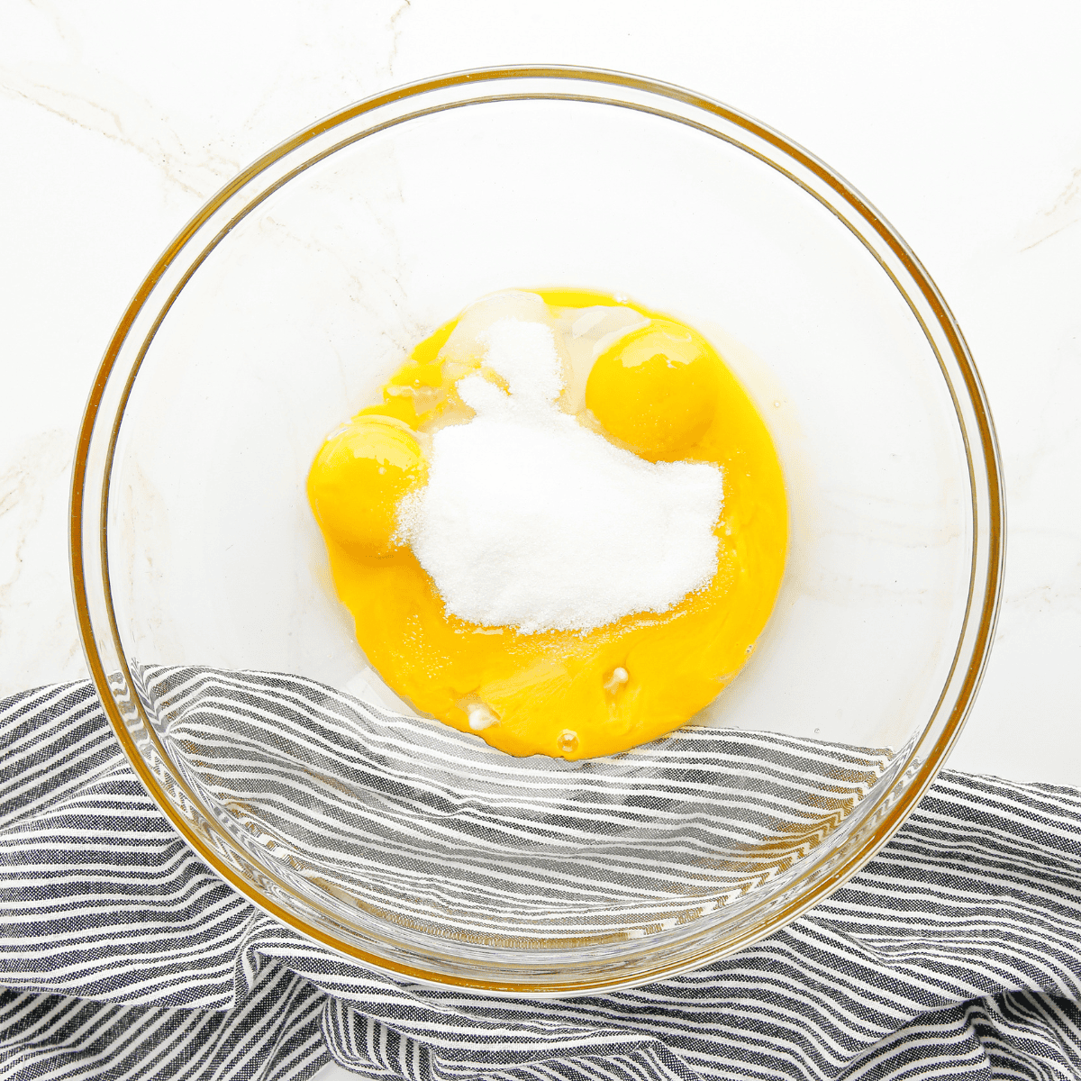 Mixing egg yolks, sugar, salt, flour, cornstarch, and vanilla in a large bowl, with air fryer tray lined with parchment paper nearby