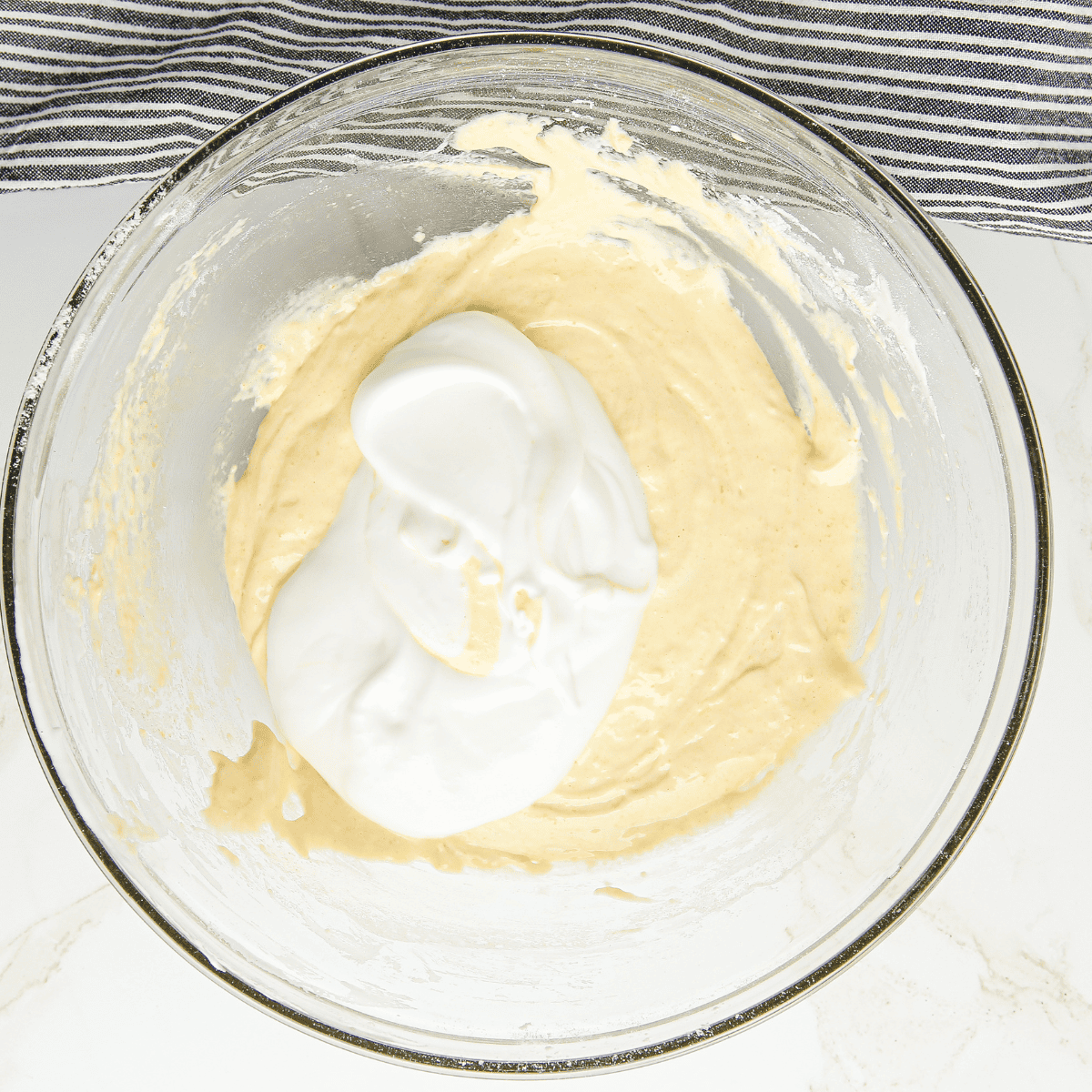 Whipping egg whites with cream of tartar and sugar, then folding into egg yolk and flour mixture to create airy ladyfinger batter.
