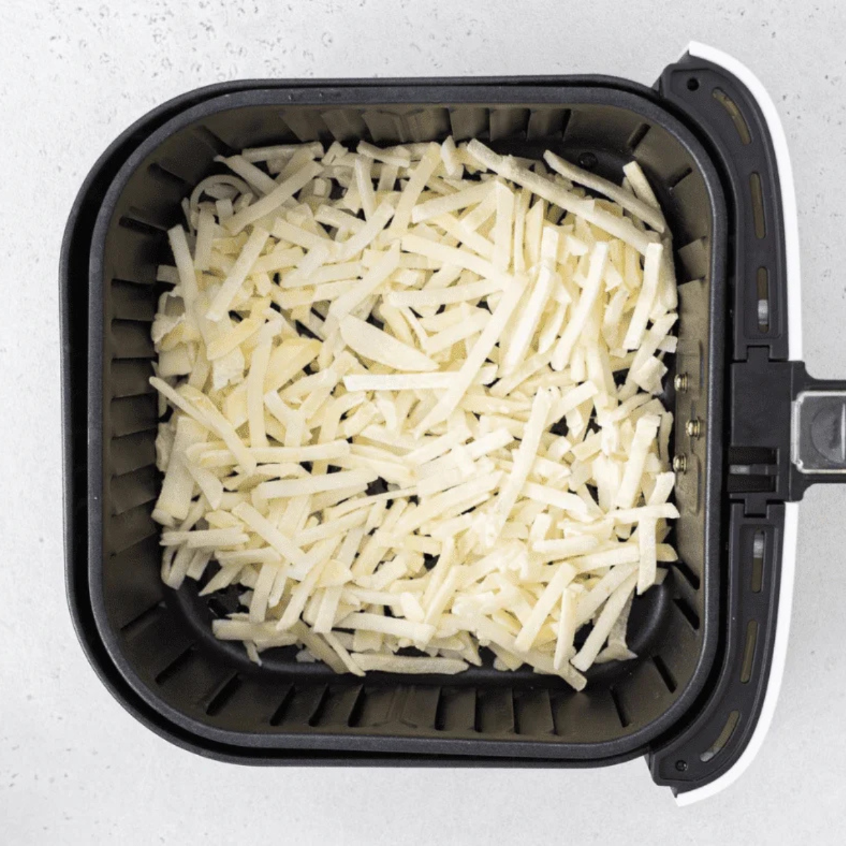 Frozen shredded hash browns crisping in the air fryer basket at 350°F