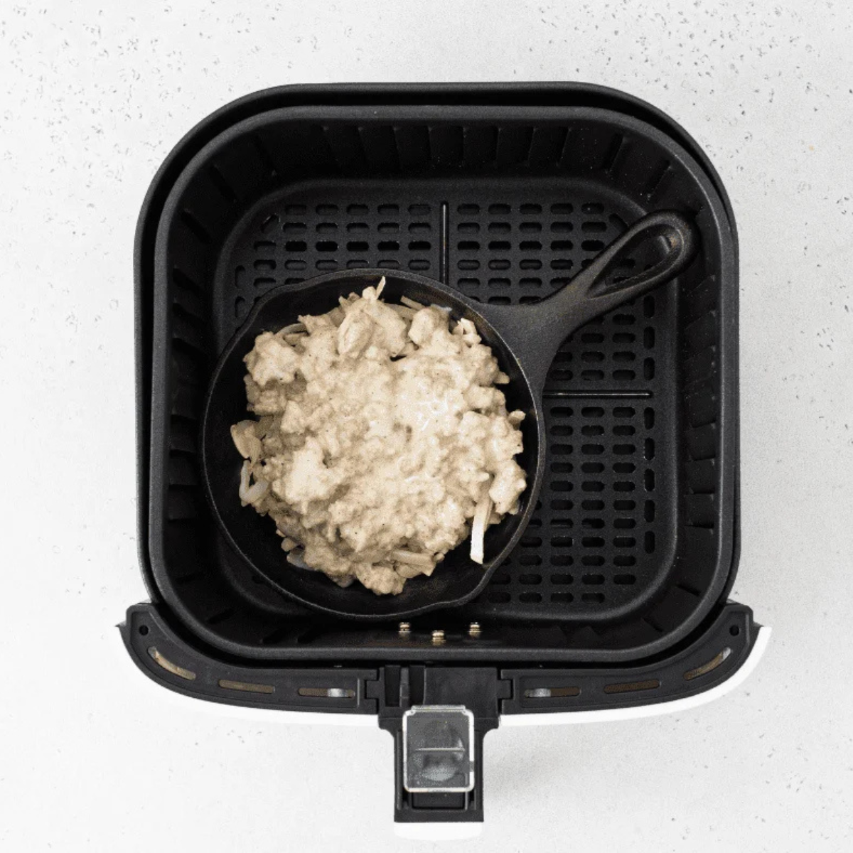 Crispy air-fried hash browns topped with sausage gravy in a baking pan, going into the air fryer