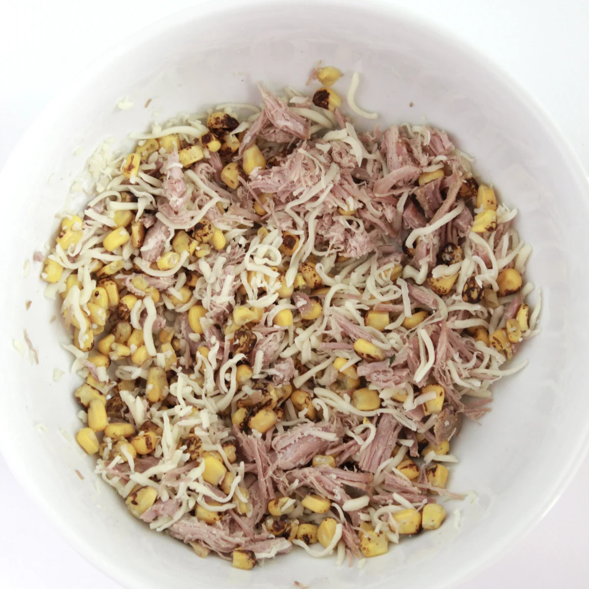Roasted corn, shredded carnitas, and mozzarella tossed with crema in a mixing bowl