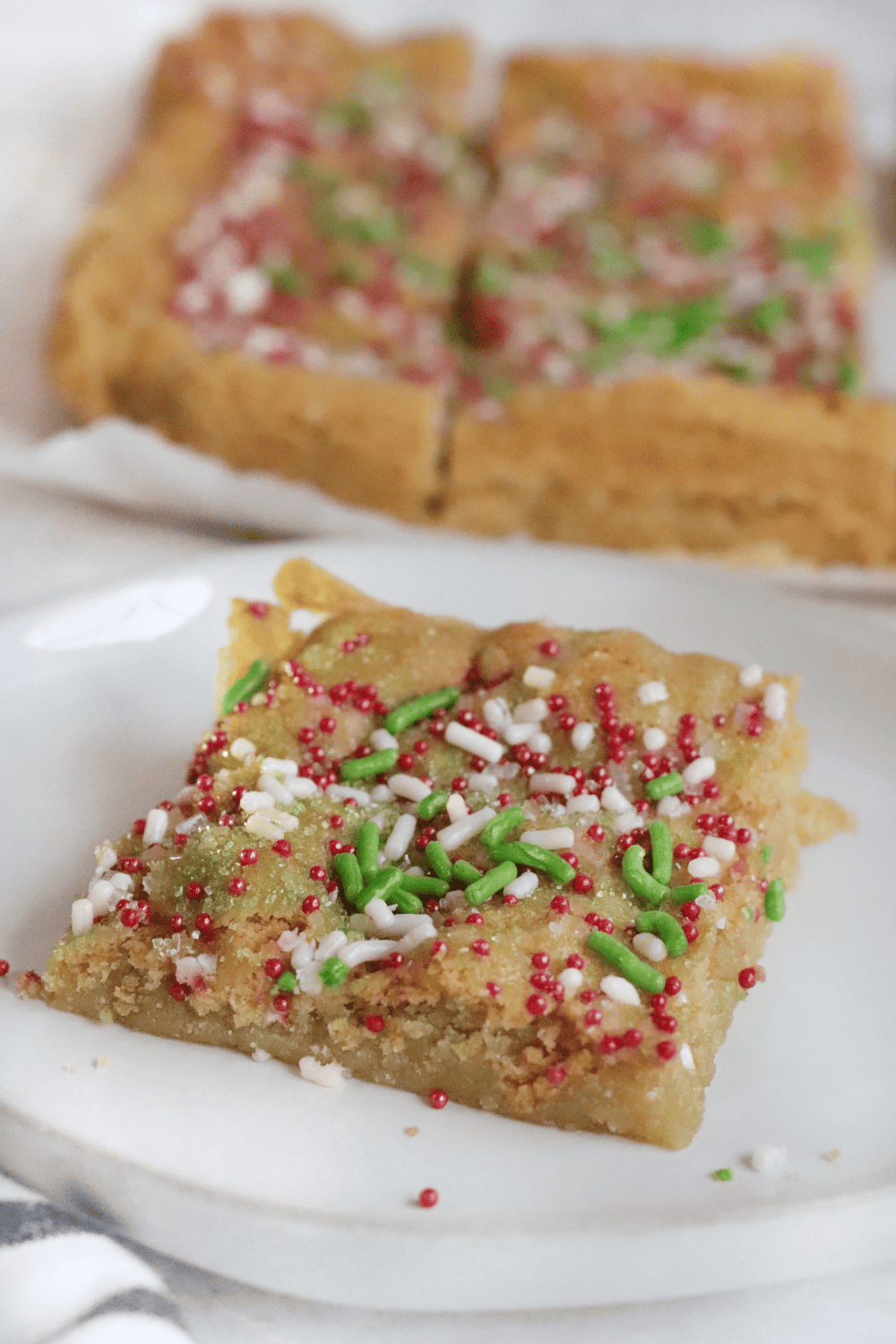 Air fryer sugar cookie bars cooling in a pan, decorated with frosting and colorful sprinkles.