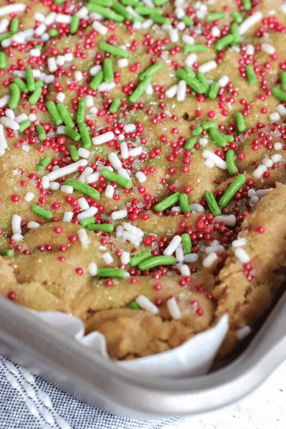 Lightly golden sugar cookie bars cooling in a pan, ready to be lifted with parchment paper and cut into squares.