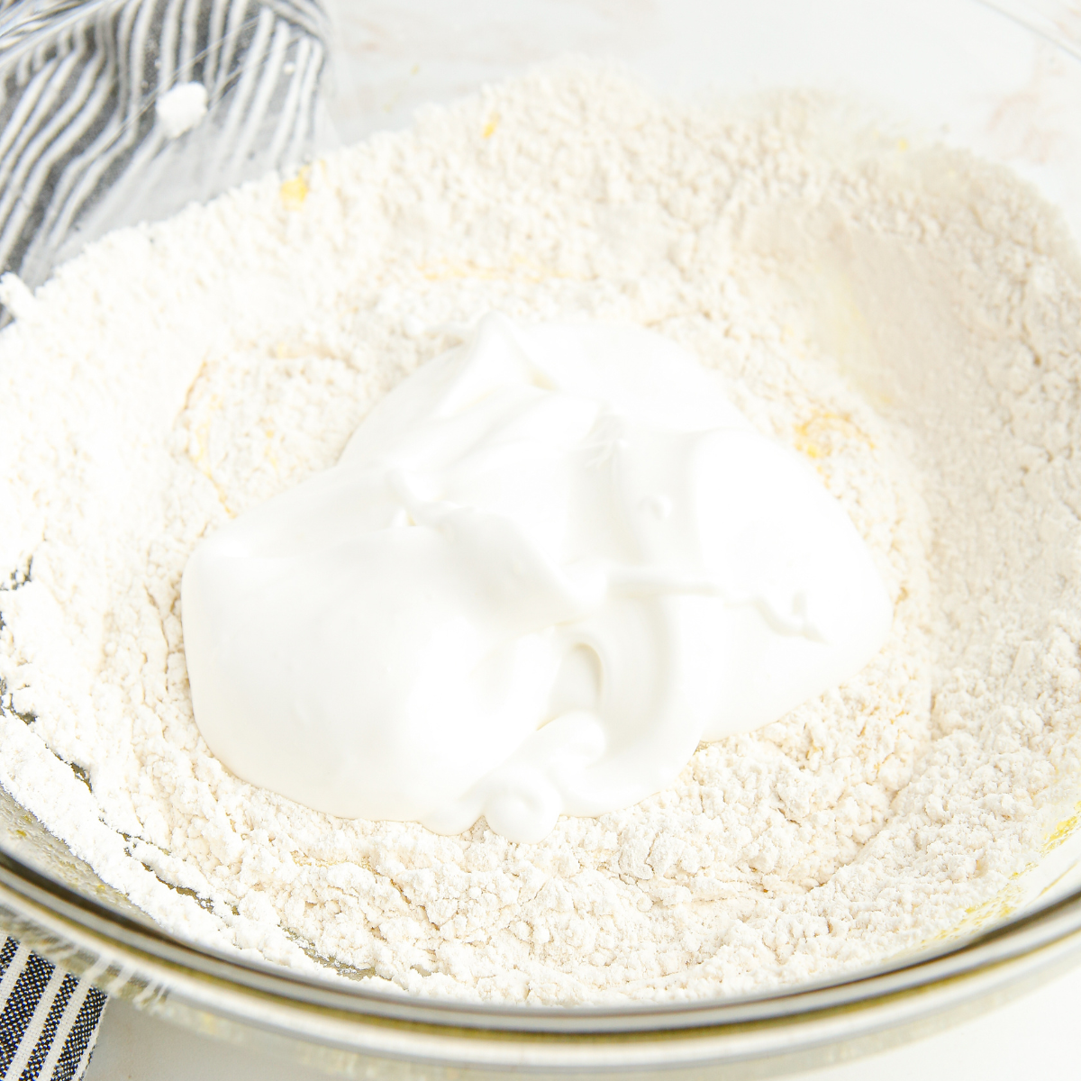 Whipped heavy cream holding a stiff peak on a mixer beater above a large mixing bowl