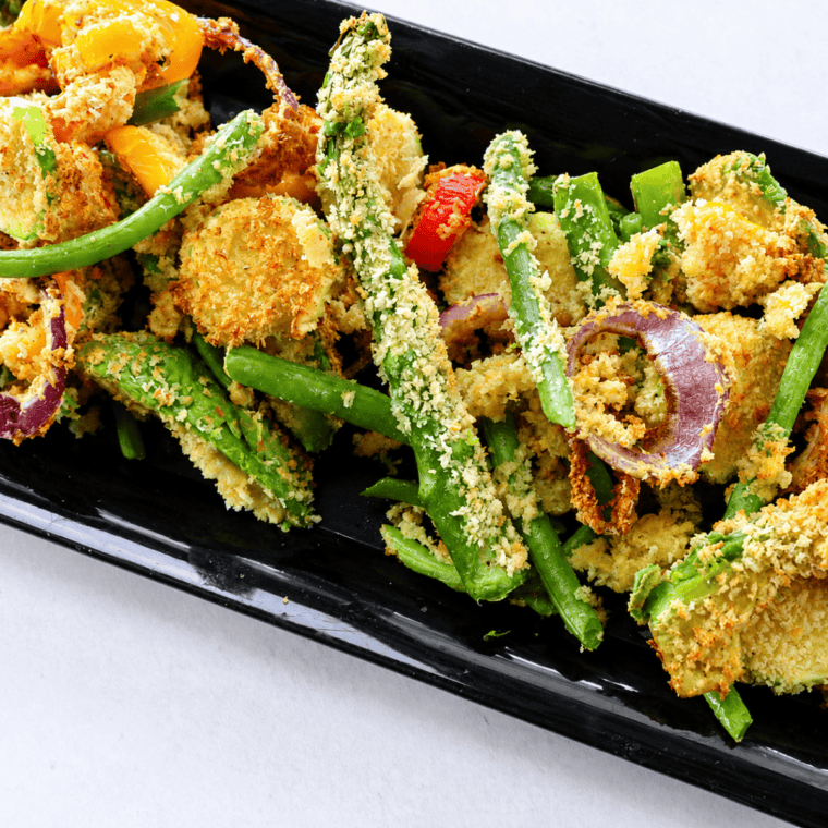 Plate of air fryer vegetable tempura with golden panko-crusted zucchini, sweet potato, and green beans beside a bowl of tentsuyu dipping sauce