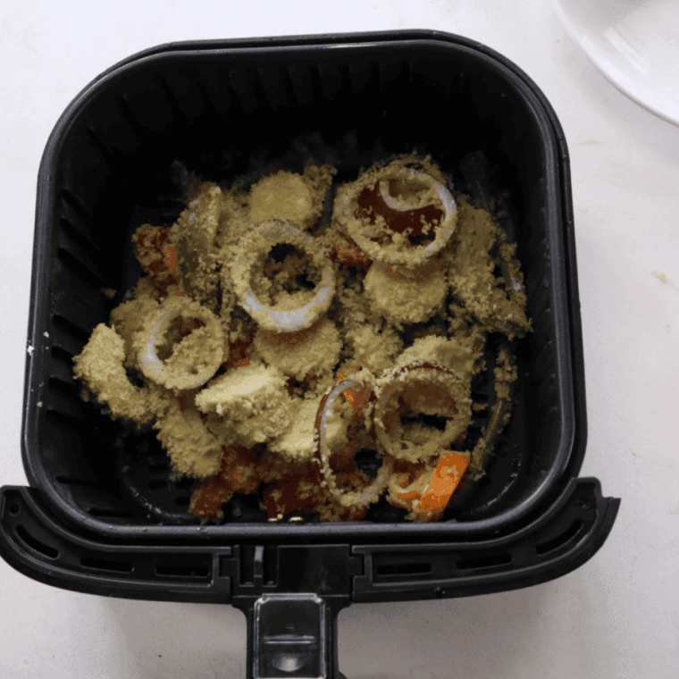 Battered vegetable tempura in a single layer in the air fryer basket, sprayed with oil before cooking