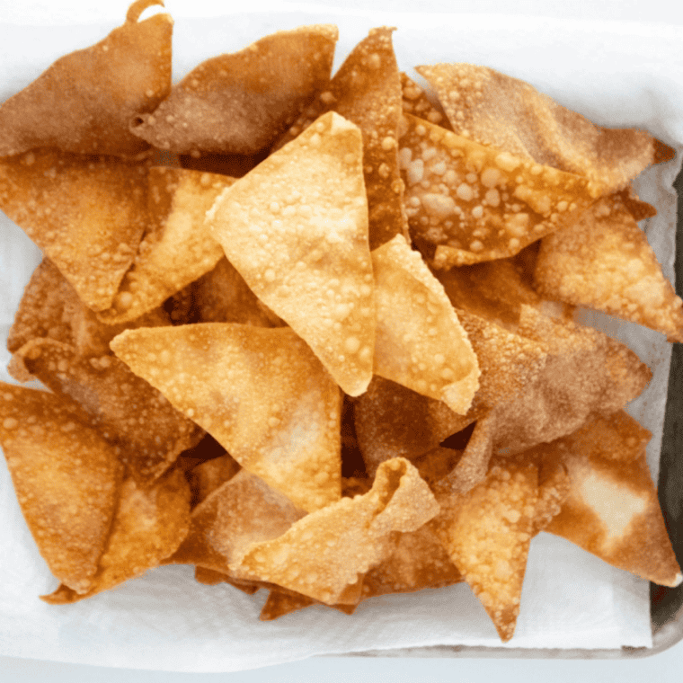 Crispy golden air fryer wonton chips piled in a white bowl with a small dish of dipping sauce.