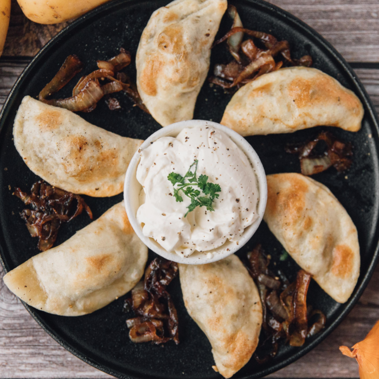 Homemade potato and cheese pierogies served with caramelized onions and sour cream on a plate.