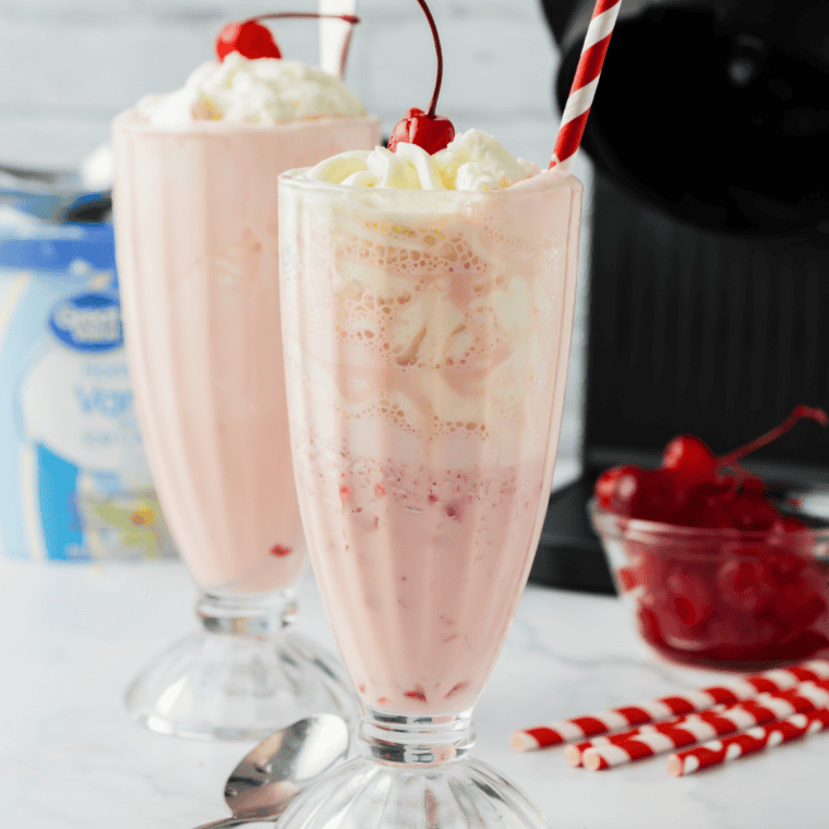 Finished strawberry milkshake poured into a glass and topped with whipped cream and a fresh strawberry
