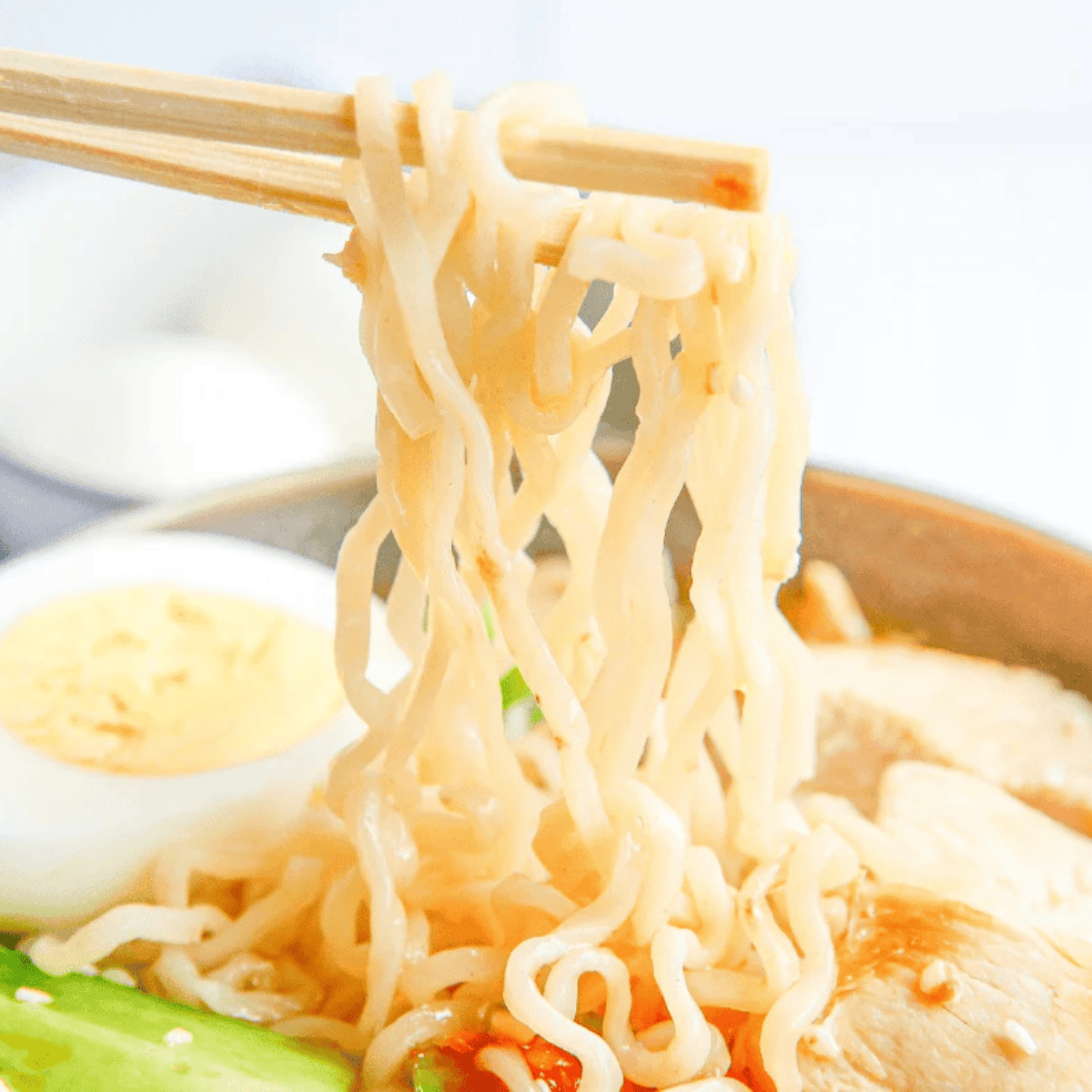 chopsticks pulling steaming noodles from a bowl of chicken ramen broth