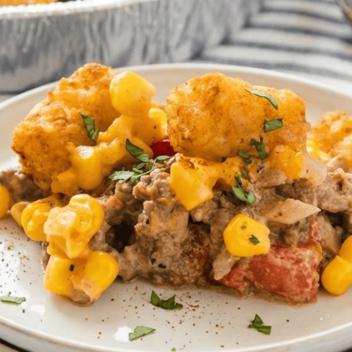 A scoop of cowboy casserole showing layers of ground beef, corn, melted cheese, and tater tots