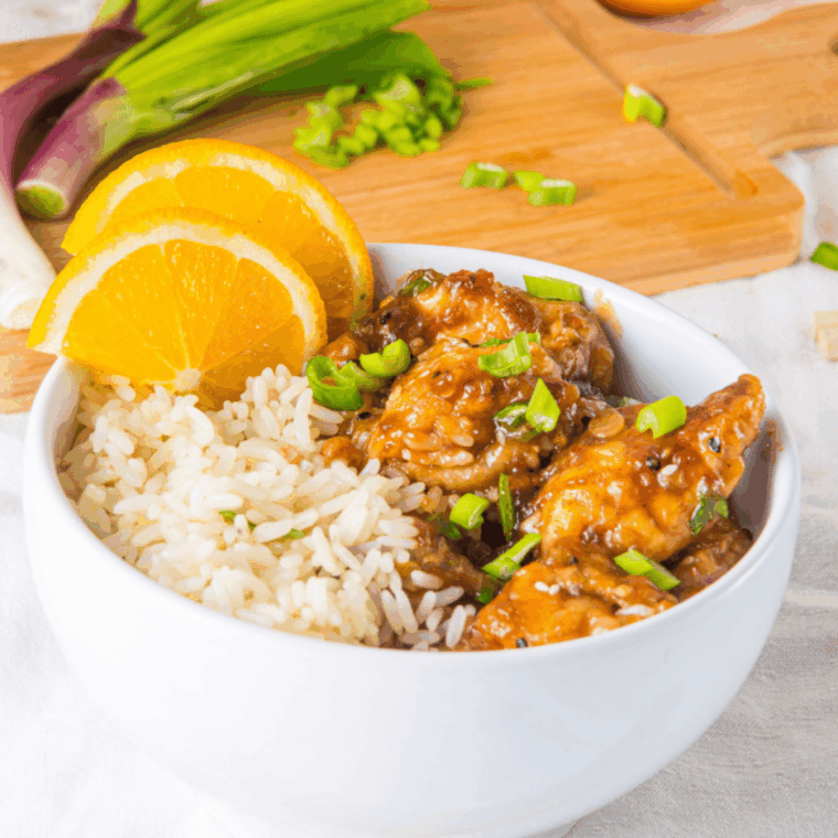 Tossing crispy chicken in thickened orange sauce and garnishing with green onions and sesame seeds