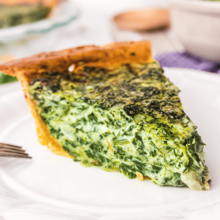 Spinach quiche sliced on a plate showing creamy egg filling with spinach and golden baked crust.