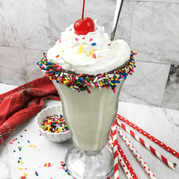 Ninja Creami vanilla milkshake on a counter topped with whipped cream and sprinkles