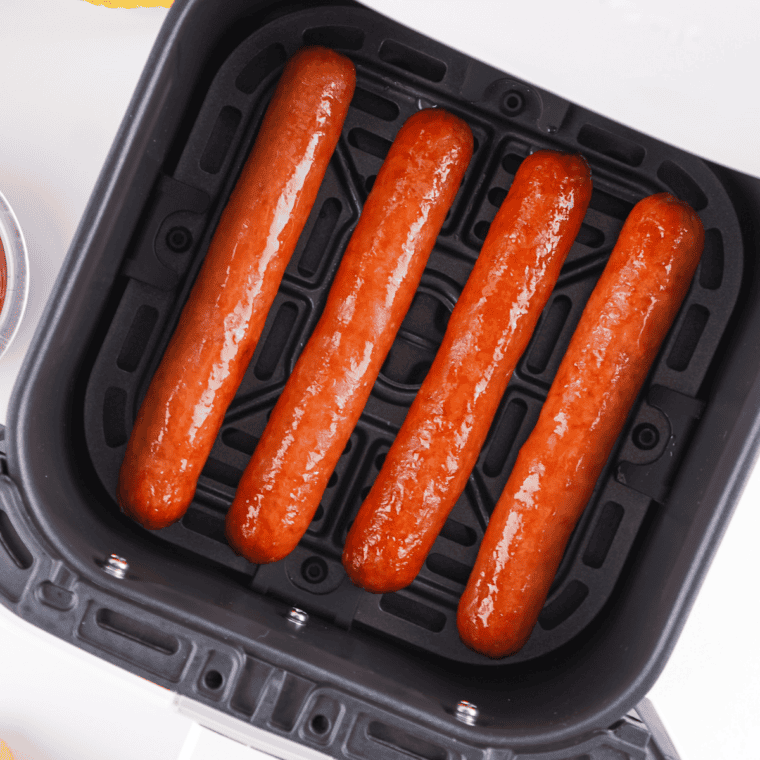 Hot dogs reheating in an air fryer basket with slightly crisped edges and warmed evenly.