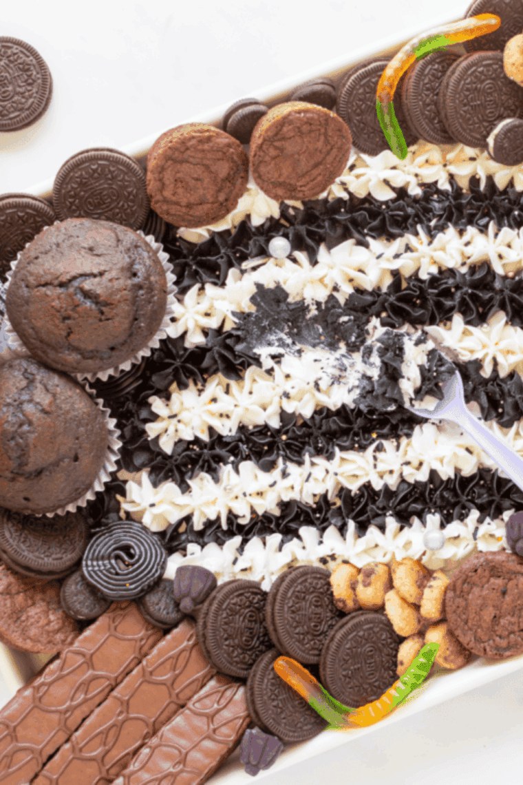 Beetlejuice-inspired buttercream board with colorful striped frosting, cupcakes, brownies, and candy arranged for Halloween.