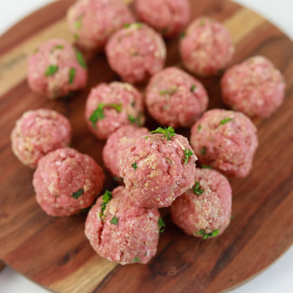 Sixteen rolled meatballs portioned with a cookie scoop on a tray