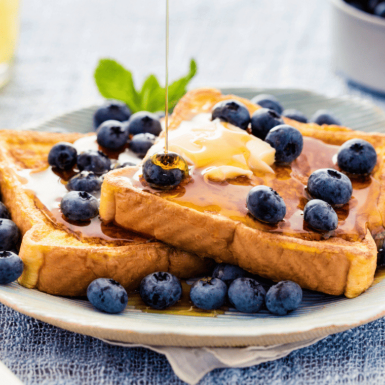 Serve and Enjoy: Air fryer eggless French toast served warm on a plate with maple syrup, fresh fruit, and powdered sugar.