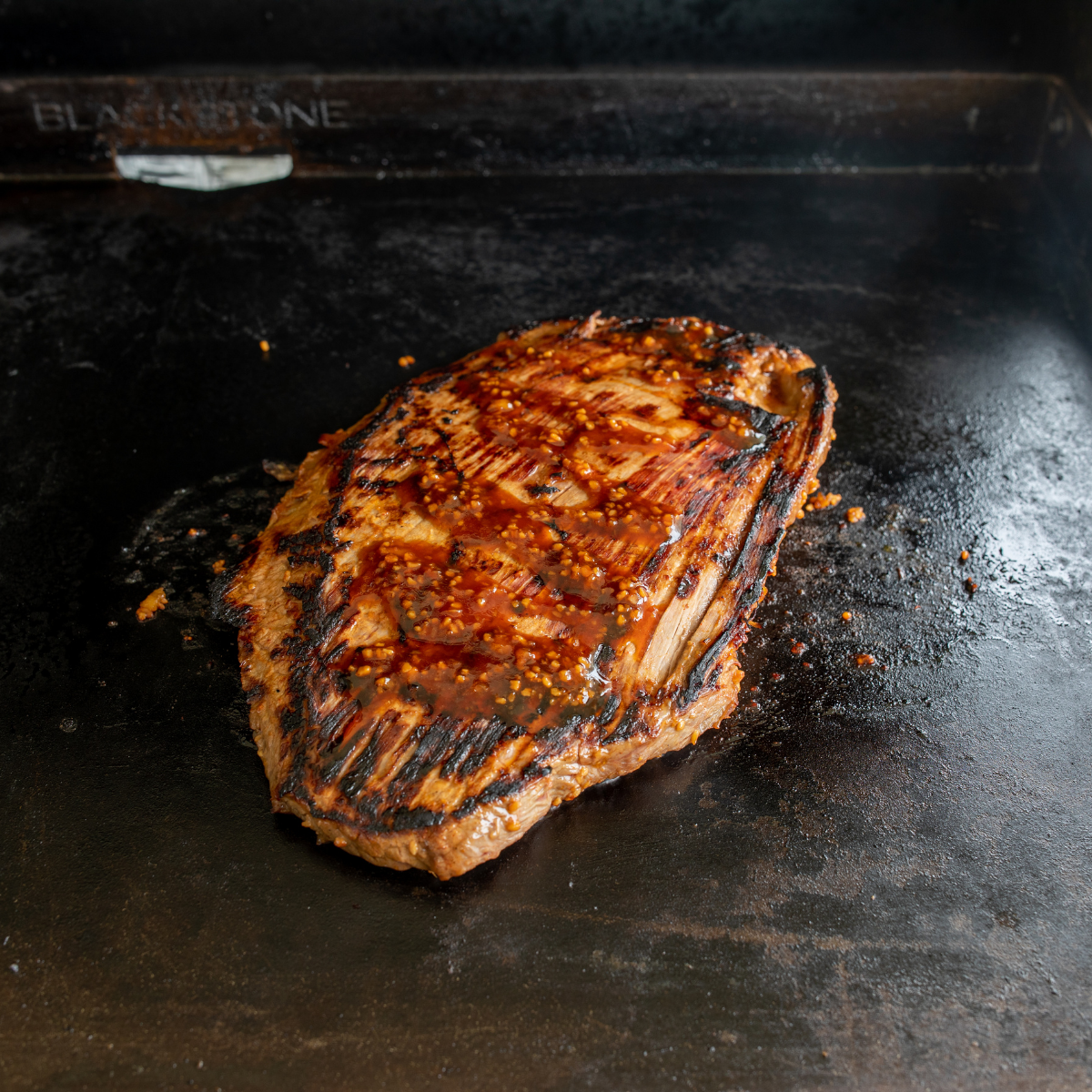 Flank steak searing on hot Blackstone griddle with strong sizzling crust forming
