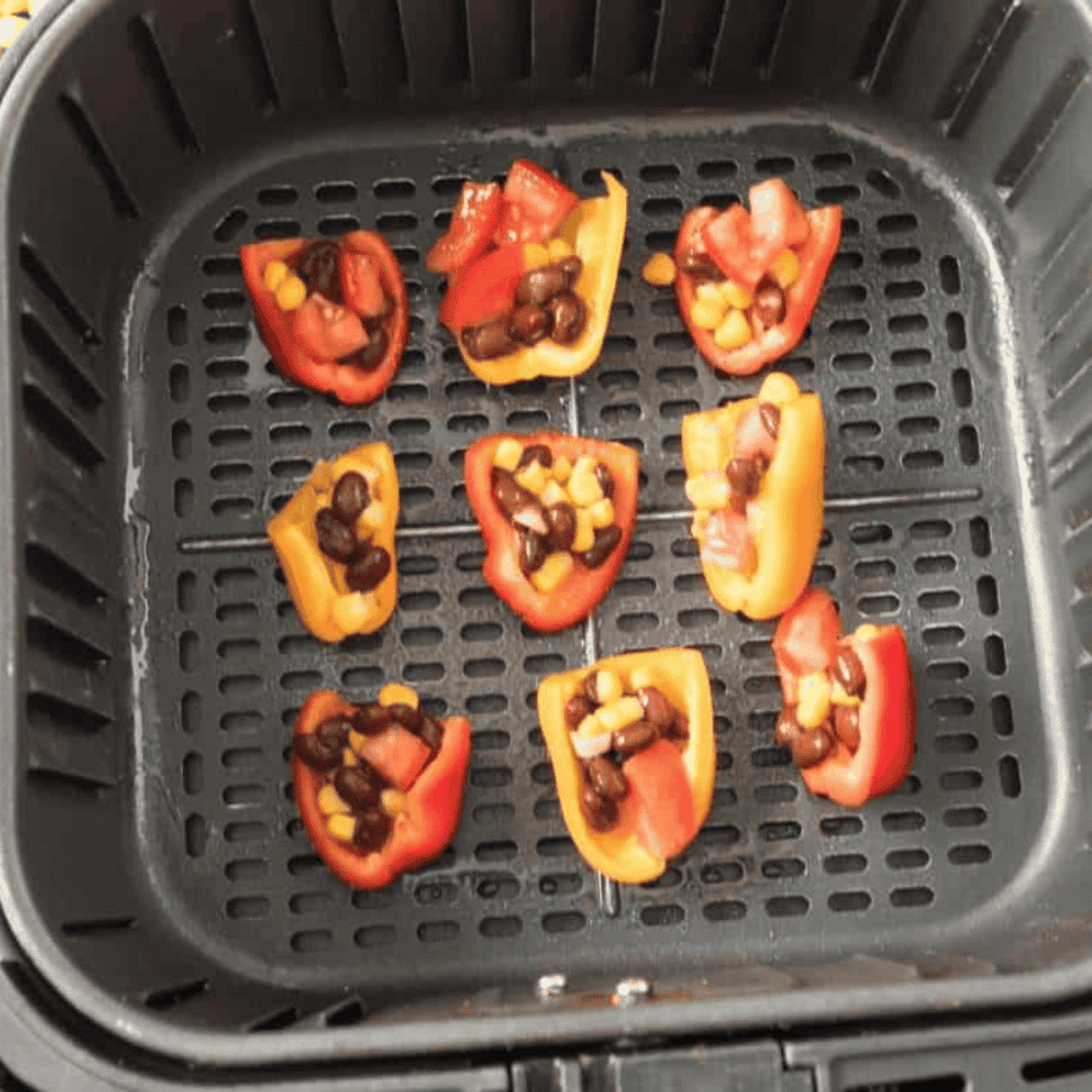 Stuffed mini peppers arranged in a single layer in the air fryer basket, spaced evenly for cooking