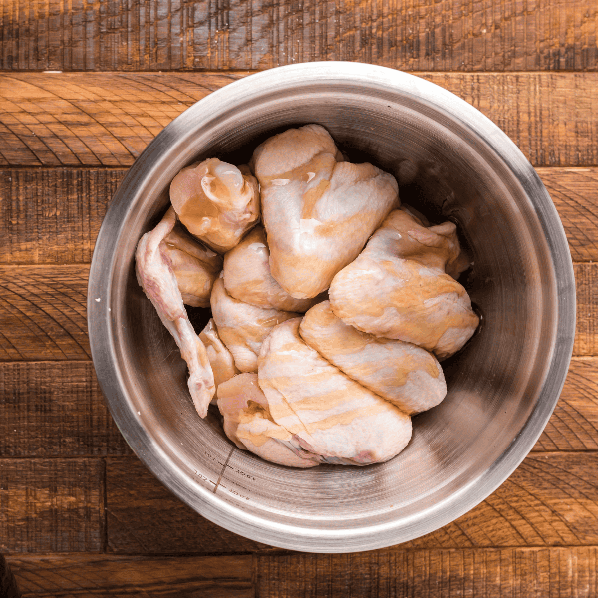 Bowl of raw chicken wings being tossed with Cajun spices for even coating.