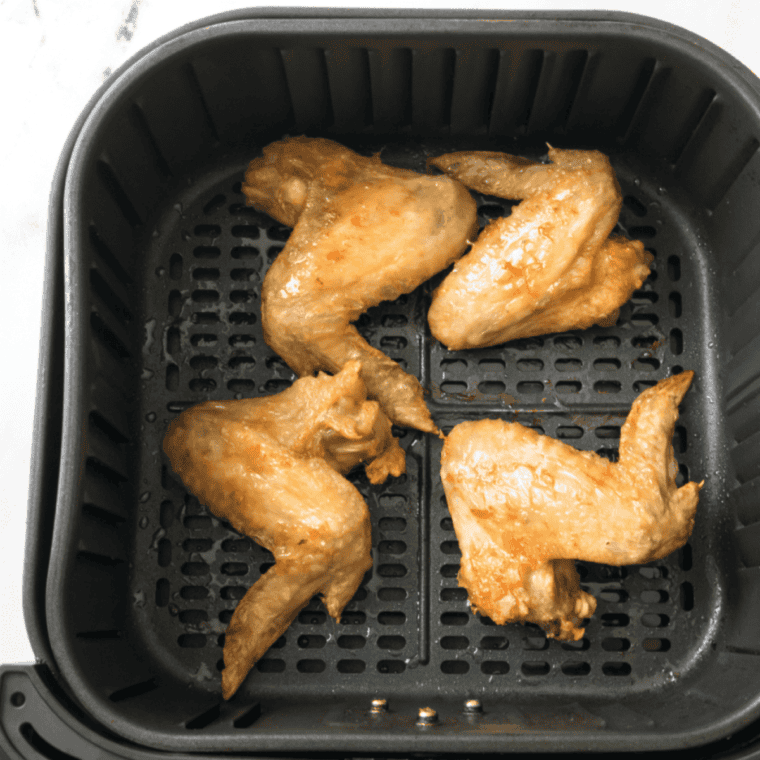 Chicken wings cooking in an air fryer, turning golden and crispy.