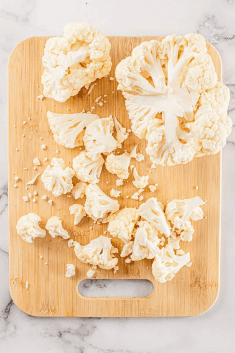 Fresh cauliflower head trimmed and cut into bite-sized florets on a cutting board, ready for roasting in a preheated oven at 425°F (220°C).