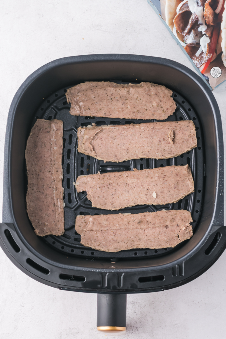 Trader Joe's gyro slices arranged in a single layer in an air fryer basket before cooking