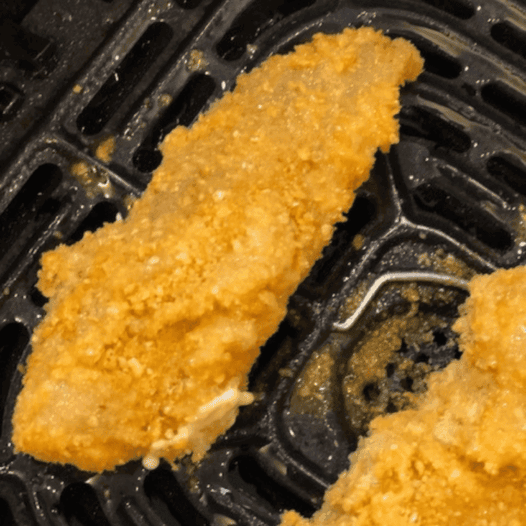 Breaded chicken tenders arranged in a single layer inside an air fryer basket before cooking.