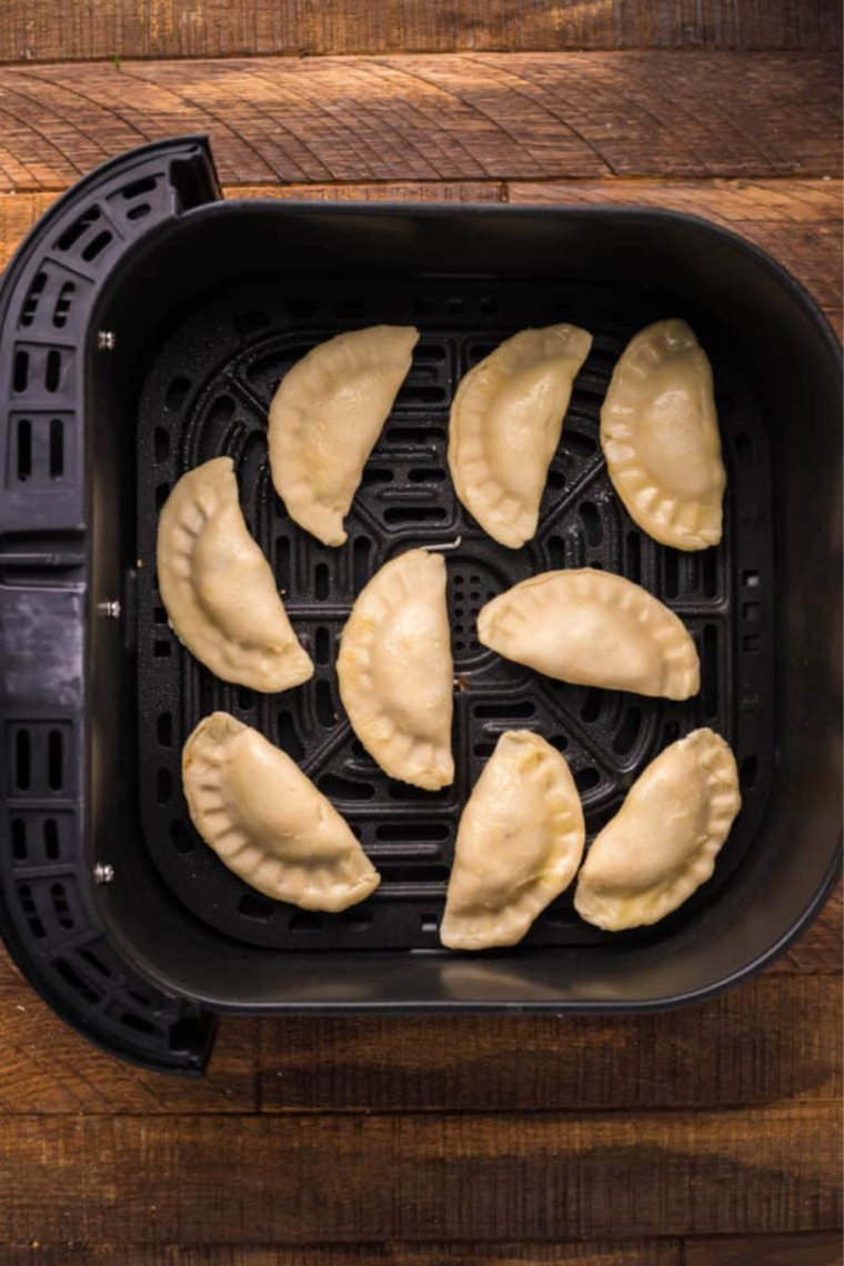 Six frozen empanadas arranged in a single layer in an air fryer basket