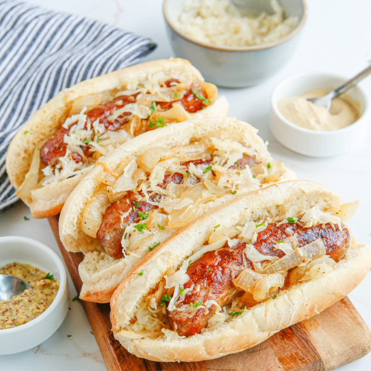 Bratwursts cooking on Blackstone griddle with caramelized onions and bell peppers