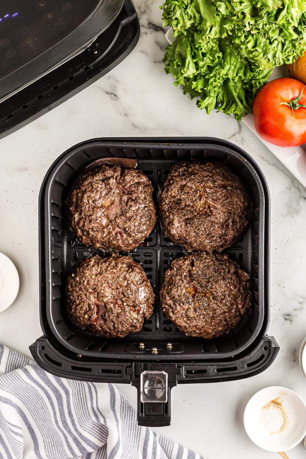 Lamb burger patties spaced evenly in an air fryer basket, ready to cook and flip halfway through.