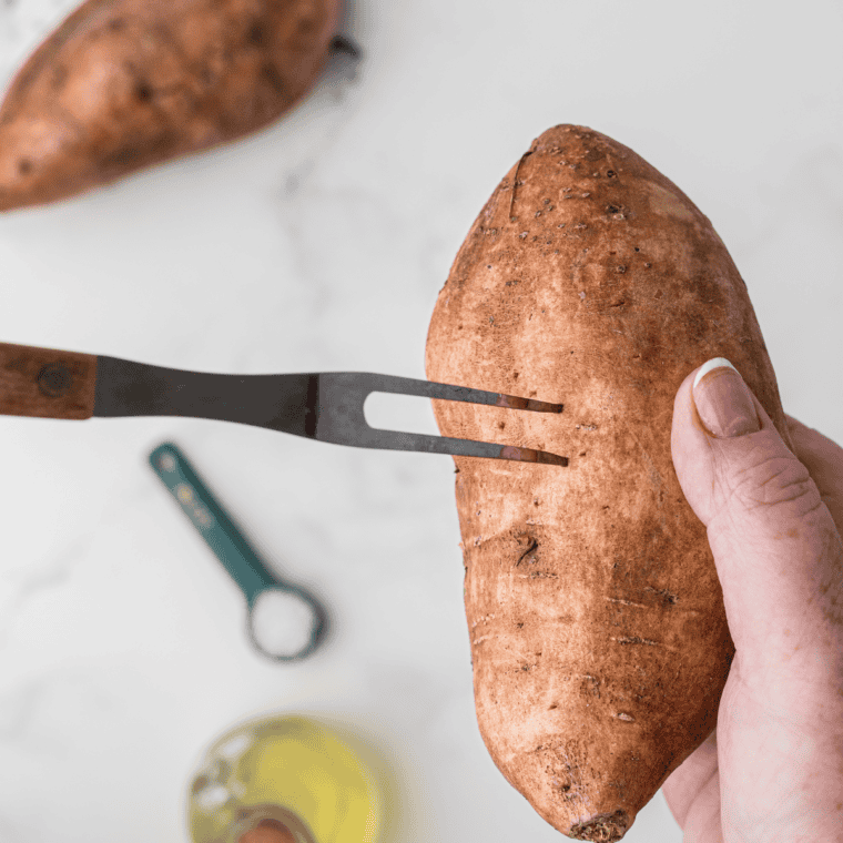 Fork piercing the skin of a raw sweet potato to let steam escape while it bakes