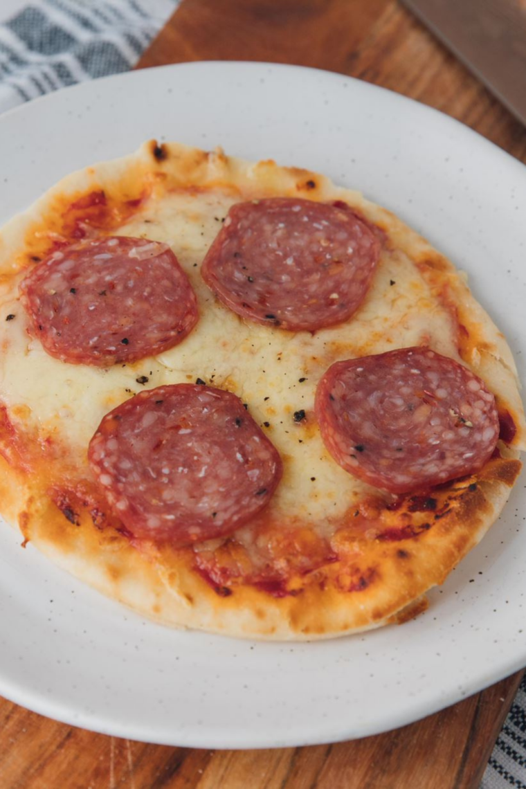 Rest and garnish
Finished air fryer pepperoni naan pizza resting in the basket with set melted cheese, topped with torn fresh basil leaves, and sliced into 4 wedges ready to serve
