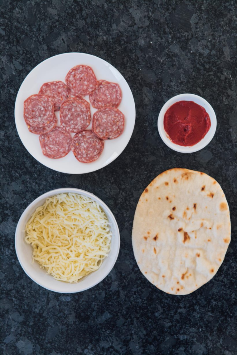 Ingredients flat lay
Air fryer pepperoni naan pizza ingredients on white marble — Stonefire naan bread, jarred pizza sauce, shredded mozzarella, pepperoni slices, Italian seasoning, and fresh basil