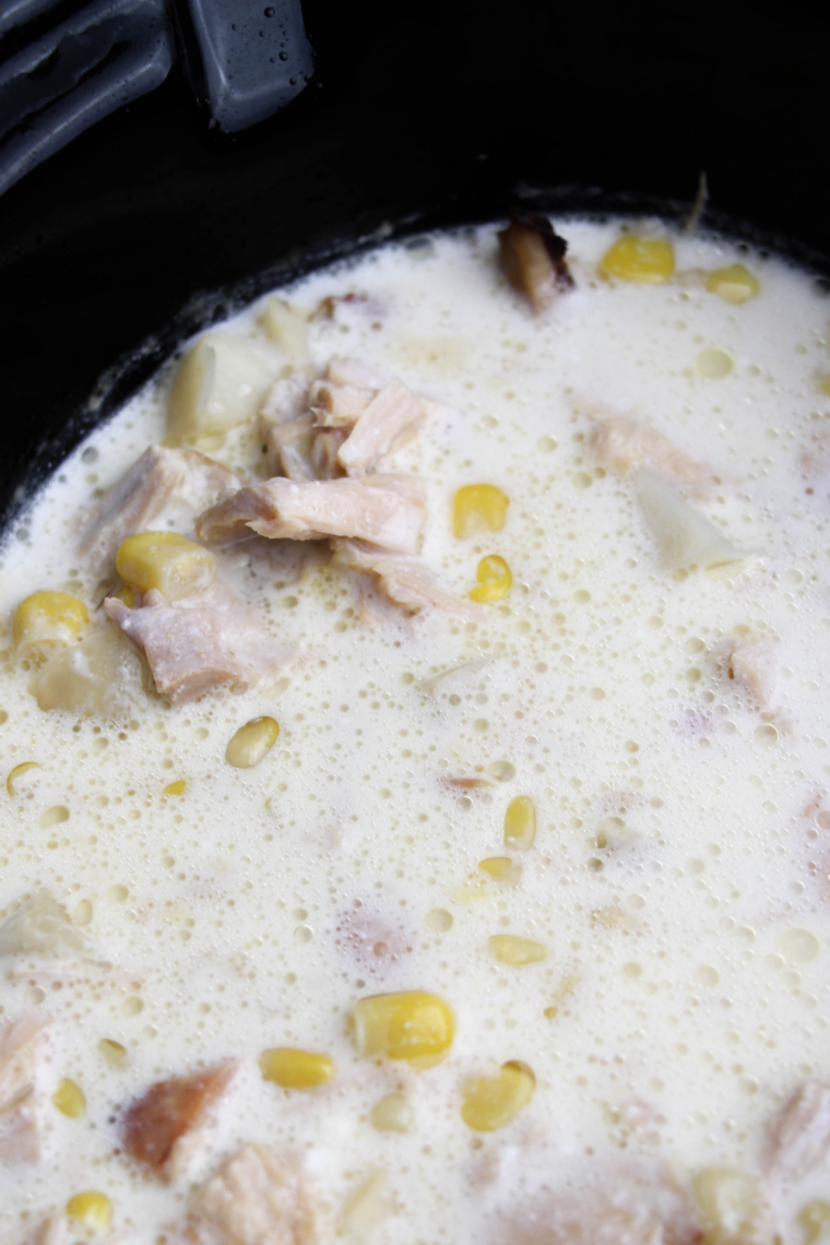 Image alt text: Cream cheese cubes melting into slow cooker turkey white bean chili being stirred with a wooden spoon