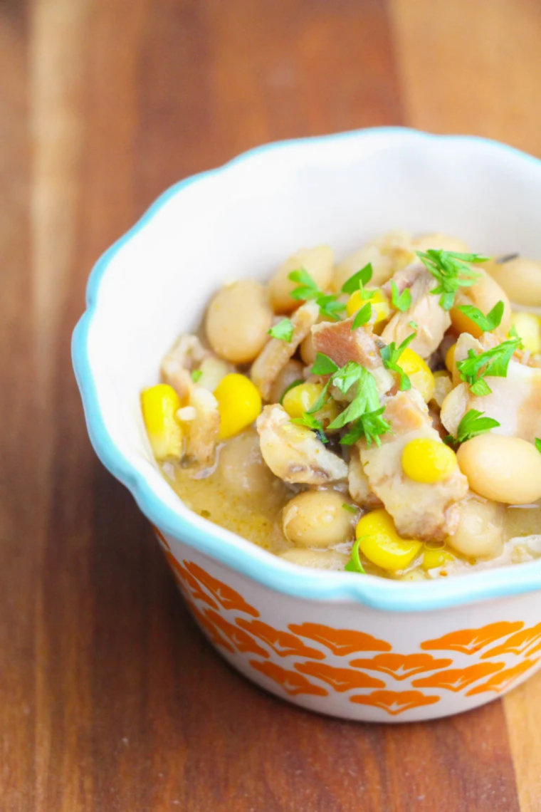 Overhead view of a bowl of creamy slow cooker turkey white bean chili with lime wedges and tortilla chips on the side