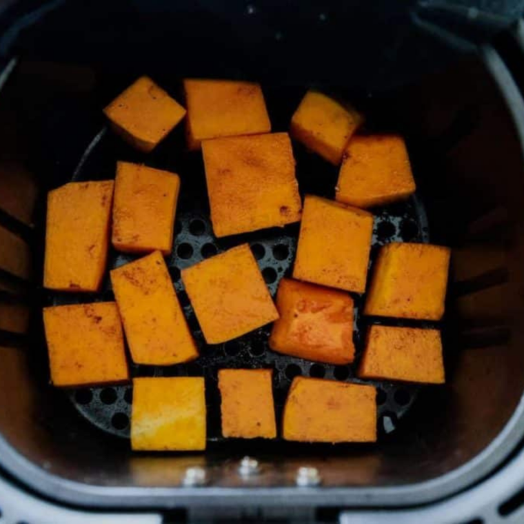 Seasoned frozen butternut squash arranged in a single layer in an air fryer basket with space between pieces
