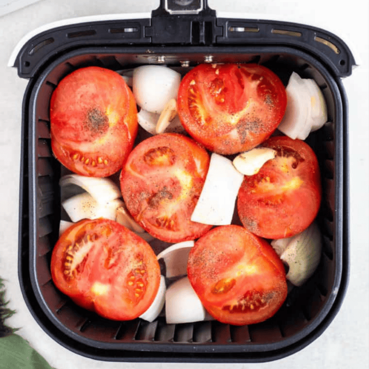 Sweet, jammy air fryer roasted Roma tomatoes on a white plate, garnished with fresh basil