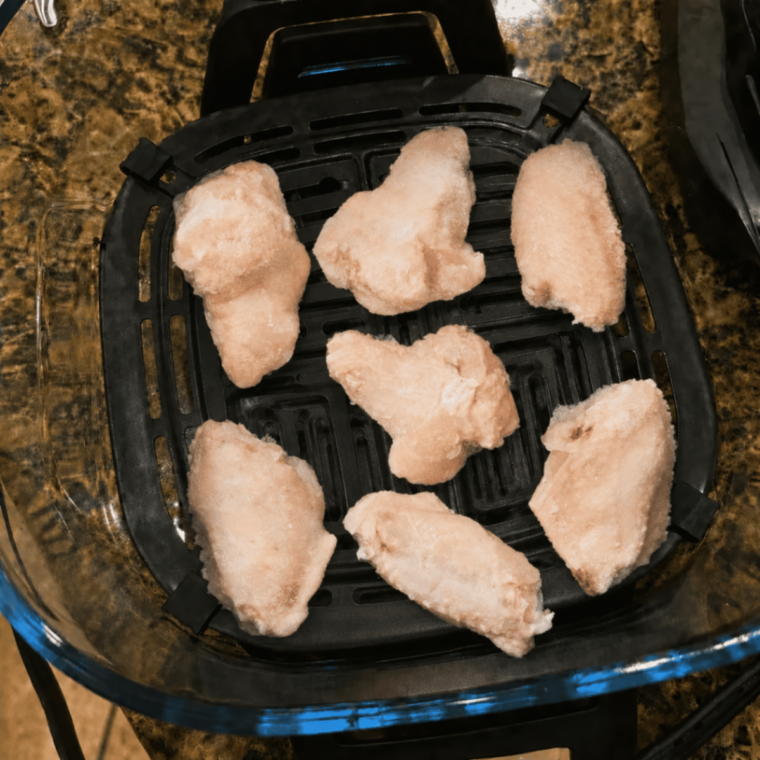 Frozen chicken wings clumped together in twos and threes on the crisper plate in the Ninja Crispi container