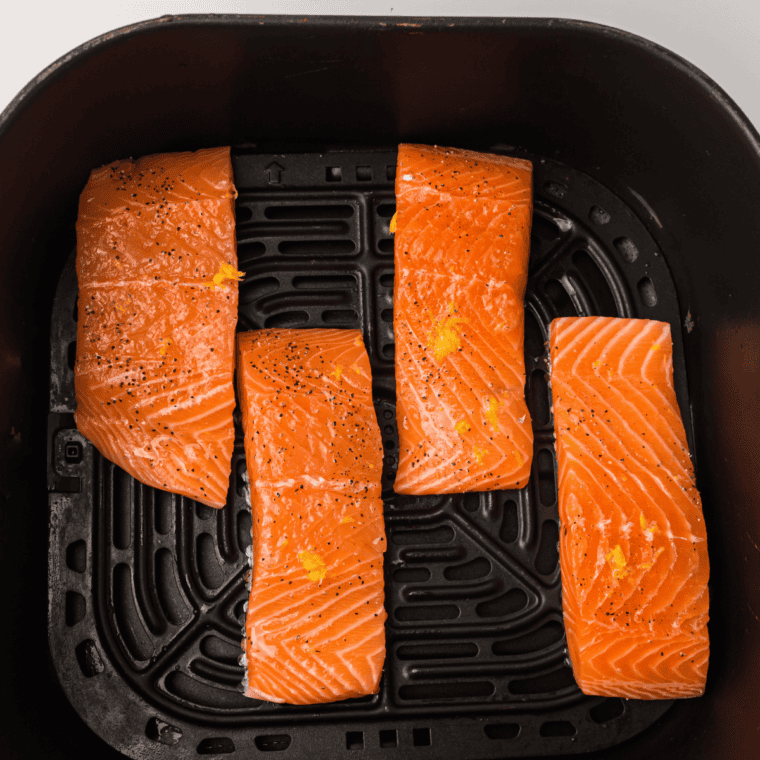 Marinated salmon fillets in an air fryer basket cooking to a golden, flaky finish.