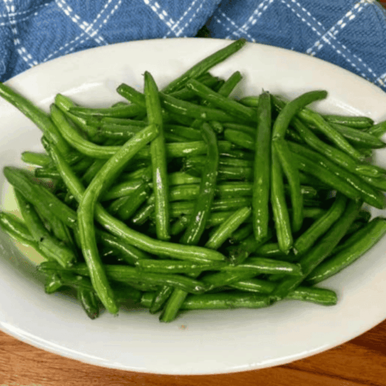 Golden air-fried green beans coated in garlic butter sauce, served hot in a bowl.