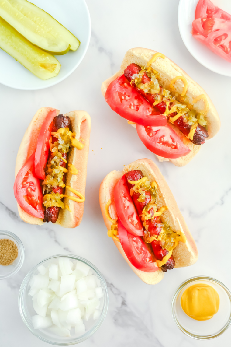Air fryer Chicago hot dog loaded with mustard, neon relish, tomato slices, pickle spear, sport peppers, and celery salt on bun.