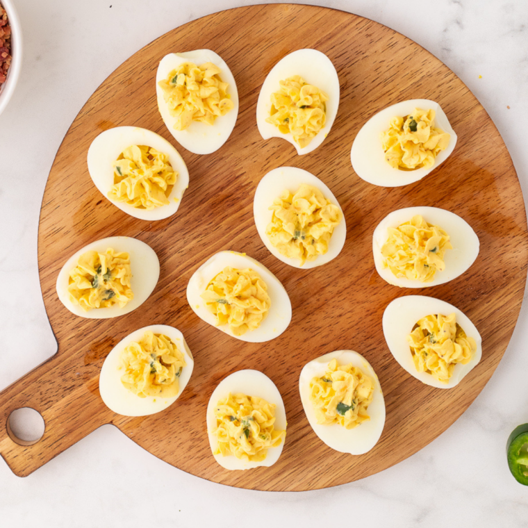 Deviled eggs without mustard on a white platter, garnished with paprika and fresh chives