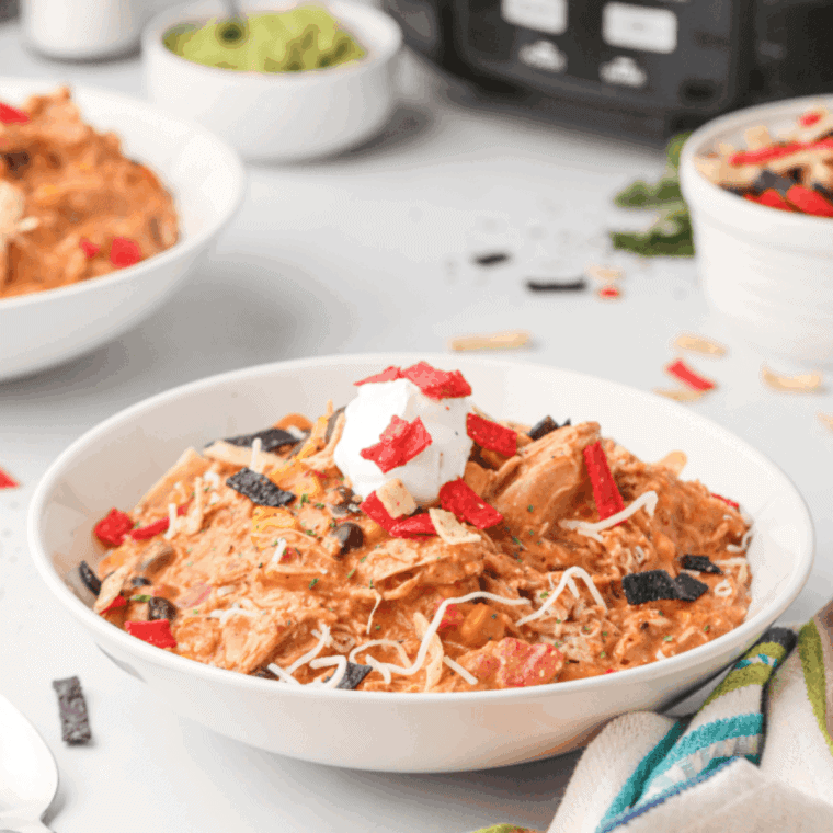 Bowl of Copycat Crockpot Jason’s Deli Chicken Chili with beans and shredded chicken, garnished with herbs.