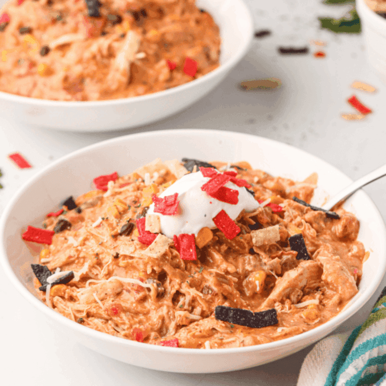 Bowl of Copycat Crockpot Jason’s Deli Chicken Chili with shredded chicken, beans, cheese, sour cream, and cilantro garnish.
