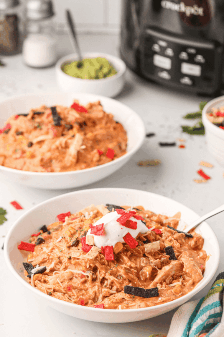Bowl of Copycat Crockpot Jason’s Deli Chicken Chili topped with shredded cheese, sour cream, tortilla strips, and fresh cilantro.