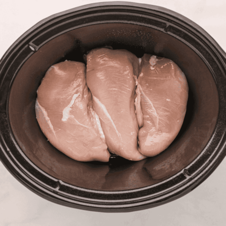 Crockpot prepared with cooking spray, chicken placed at the bottom, and other ingredients added and lightly stirred.