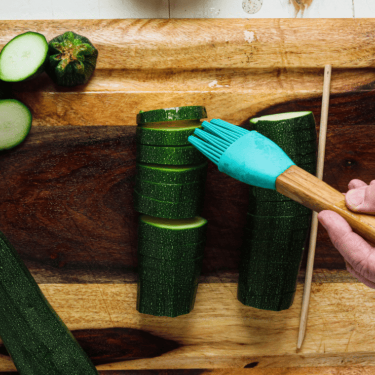 Zucchini being brushed with olive oil and seasoned with garlic, salt, pepper, and paprika, with oil and spices between slices.