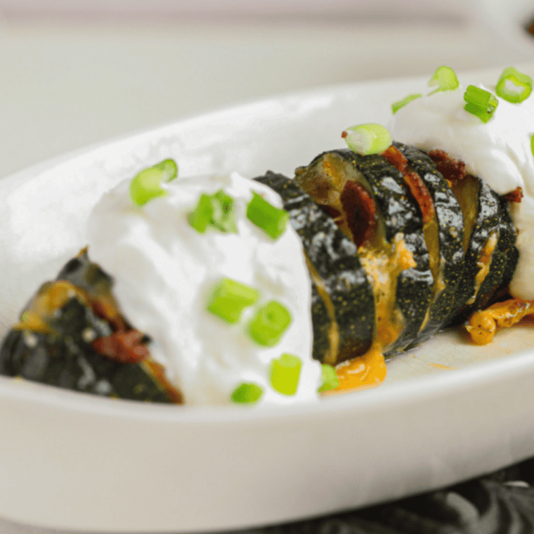 Golden-brown Hasselback zucchini in an air fryer, sliced and topped with herbs and melted cheese.